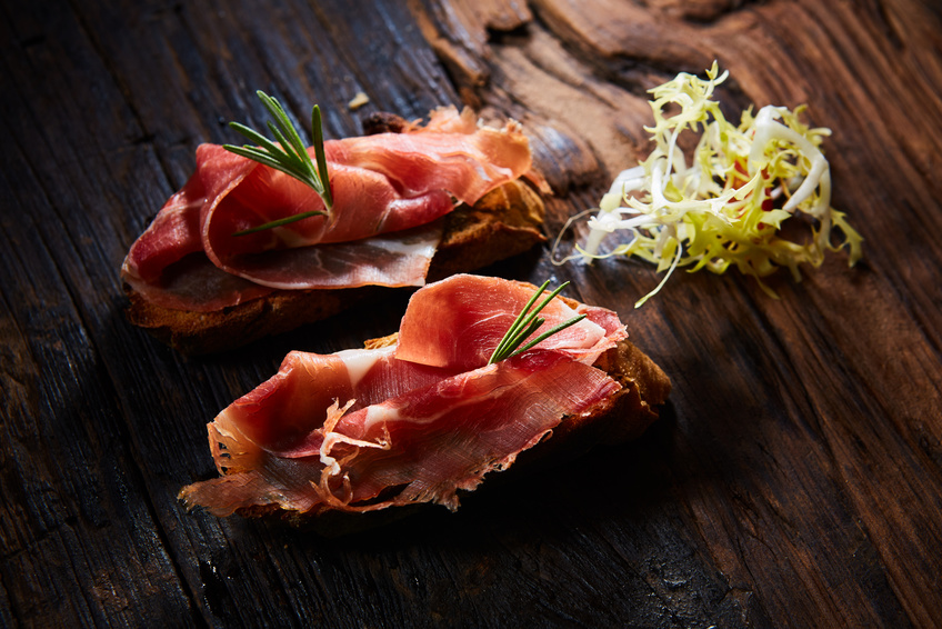 Two slice of Spanish tapas with jamon on a wooden table